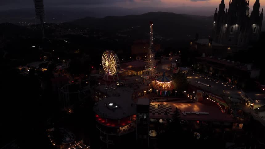 Amusement park containing a castle stands on a hill overlooking a valley under a red tinted sky before dawn