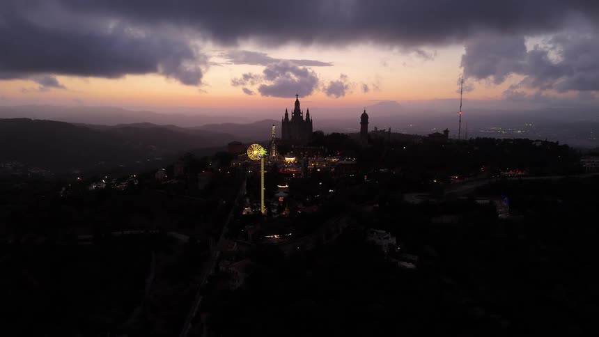 Domed buildings and structures decorated by light patterns stand on a mountain overlooking a valley under a red tinted cloudy sky