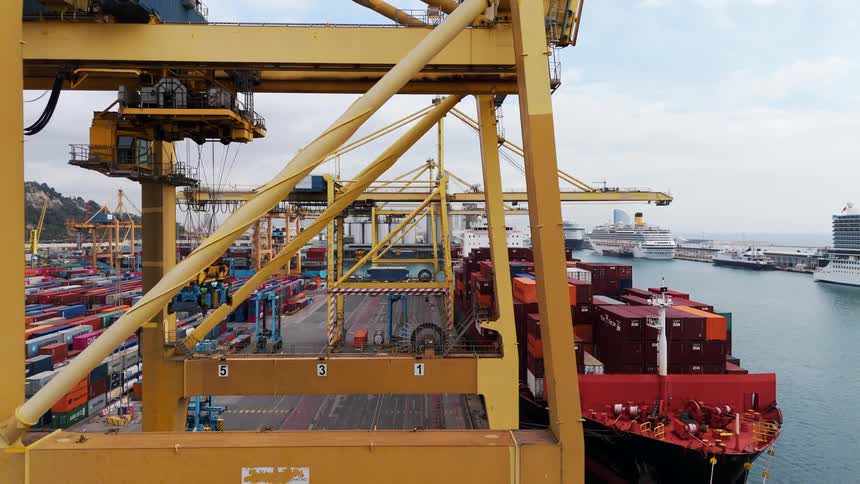 Container ship sits next to the loading cranes at the loading dock located near a mountain on a cloudy day