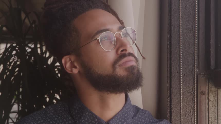 Based on the video a man with a beard and glasses is looking out a window he appears to be deep in thought