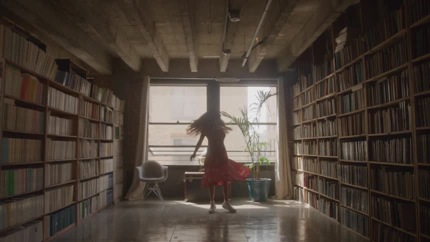 Based on the video a woman in a red dress is dancing in a library with floortoceiling bookshelves she spins around joyfully before stopping to look out the window