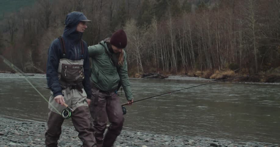 Two anglers walking by the river with fishing rods