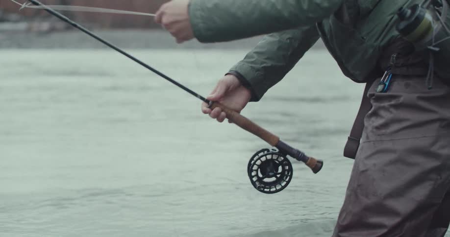 A person stands in a river and works with a fishing rod and reel