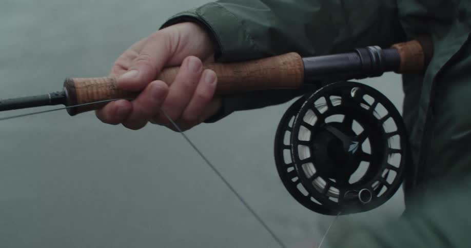 Hands holding a fishing rod with reel by the river