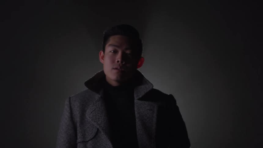 A male fashion model strikes poses and makes facial expressions as he puts on a coat and photo flashes go off around him