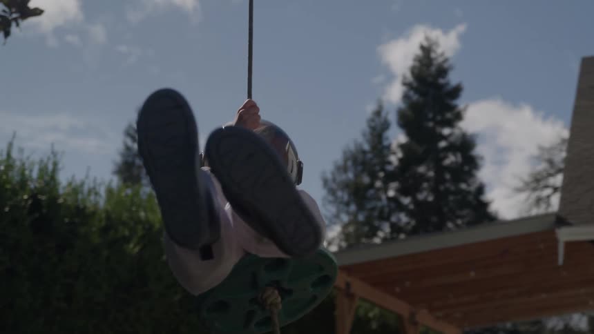 A person in a space suit swings on a rope swing in a backyard