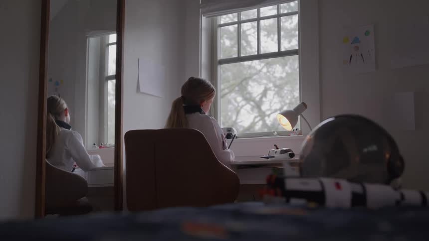 The girl is writing at her desk by the window