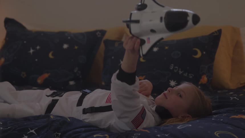 Girl lying down dressed as an astronaut holding a toy rocket