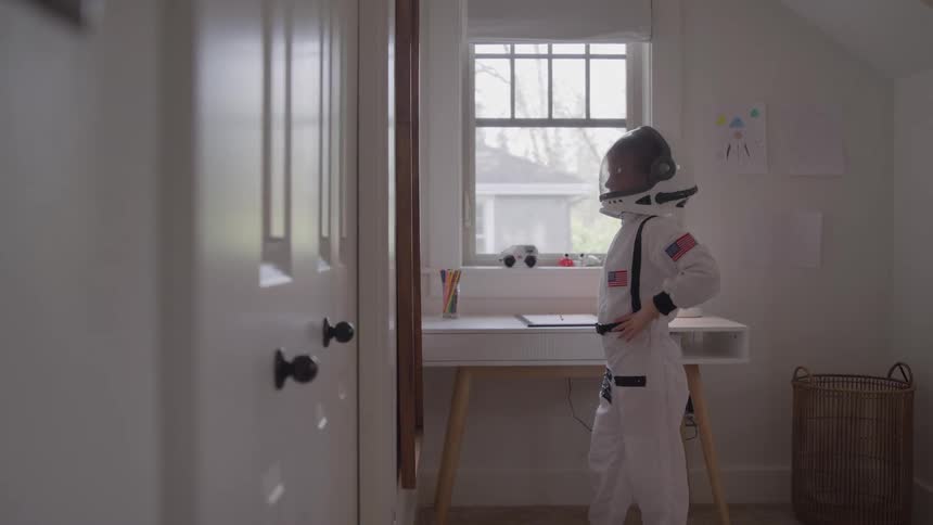 A young girl in an astronaut costume puts on her helmet in her bedroom