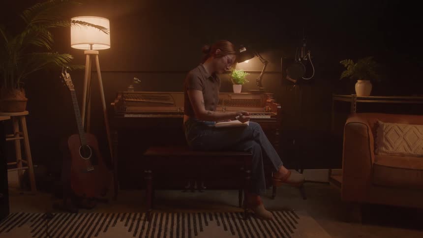 The woman sits by the piano writing in a notebook