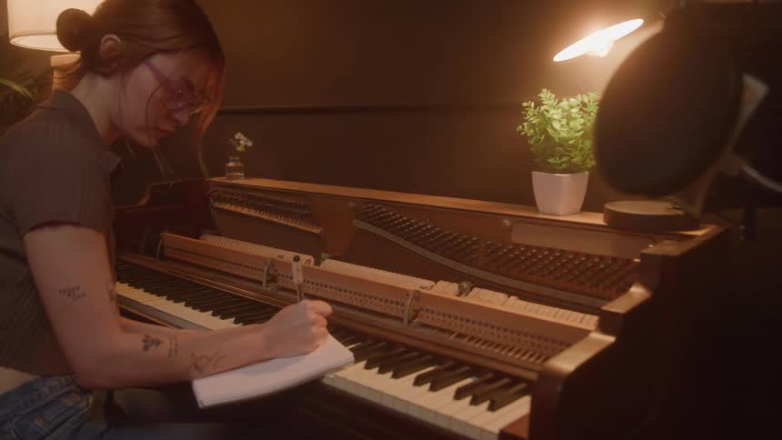 The woman leans her notebook on the piano and writes in a notebook