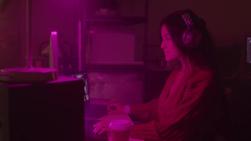 A young girl sits at a desk in a room works on a computer and wears headphones
