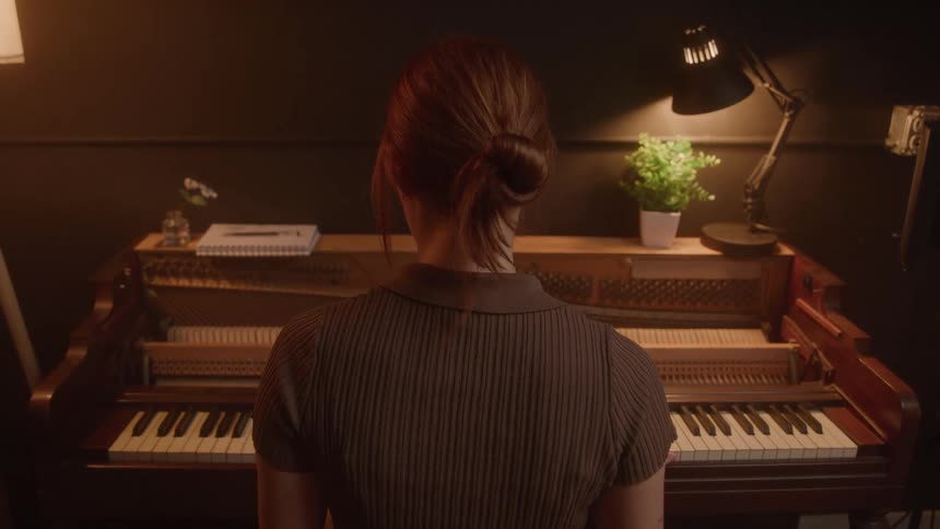 A woman with her hair in a bun and wearing a brown shirt is shown from behind as she looks at a vintage piano with its internal mechanisms exposed in a dimly lit room