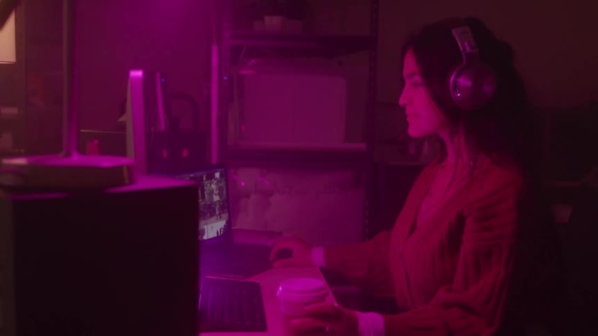 Woman with headphones in front of a computer in a room with pink