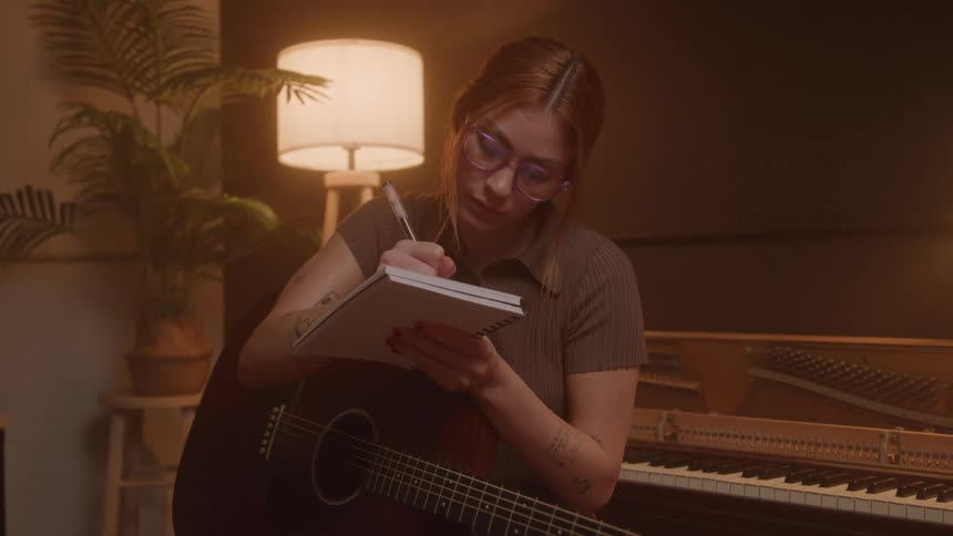 Woman plays guitar and takes notes in a notebook