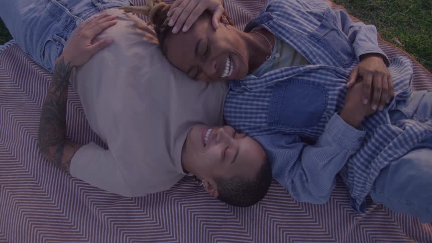 A happy couple cuddles and smiles while lying on a striped blanket in a park