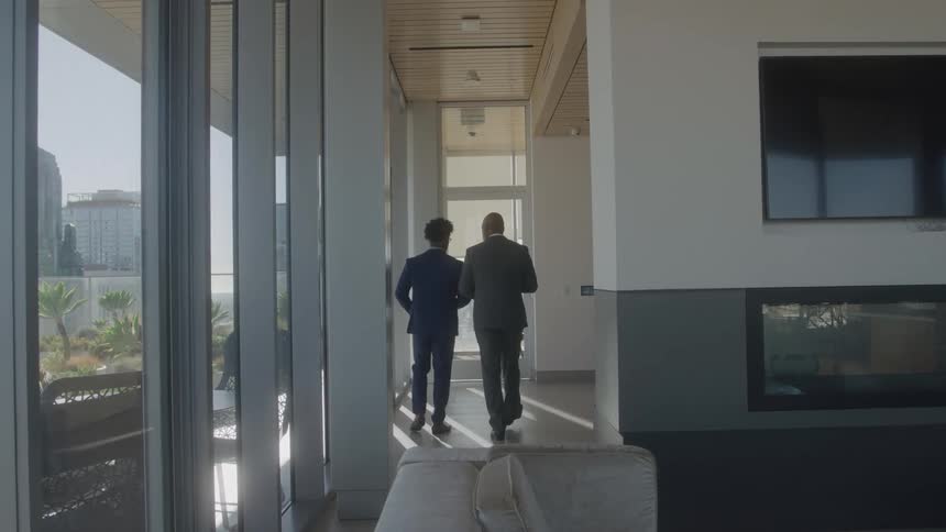 Two men in suits walk down a hallway