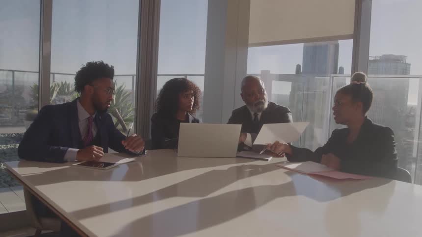 Four business colleagues have a meeting at a conference table in a modern sunlit office with a city view
