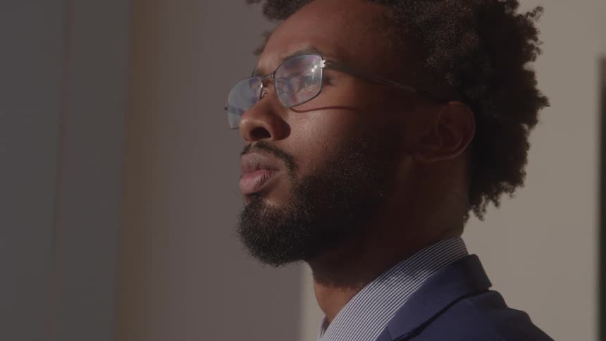 In a sunlit close up a pensive businessman with glasses looks thoughtfully into the distance