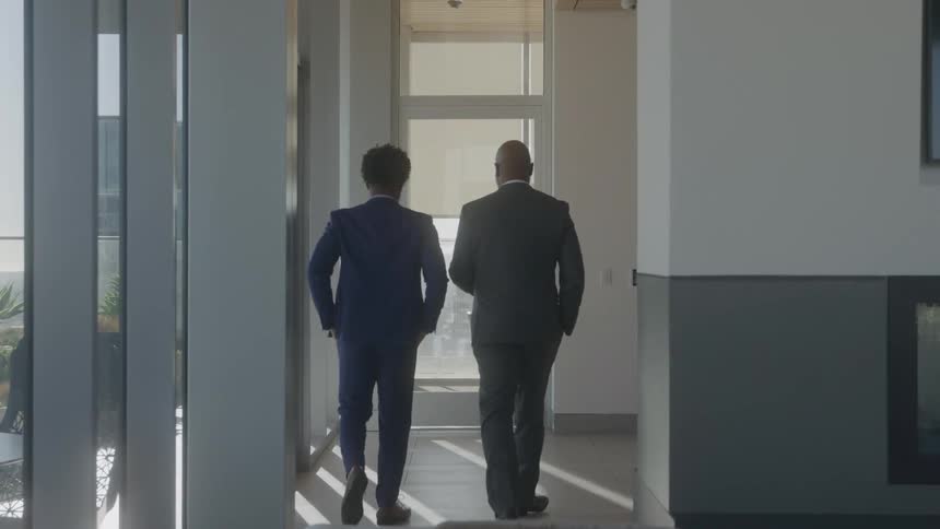 Two men walk through the office hallway talking