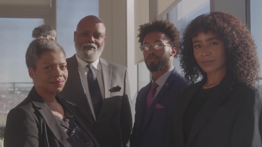A group of four people in business clothes stands and looks at the camera