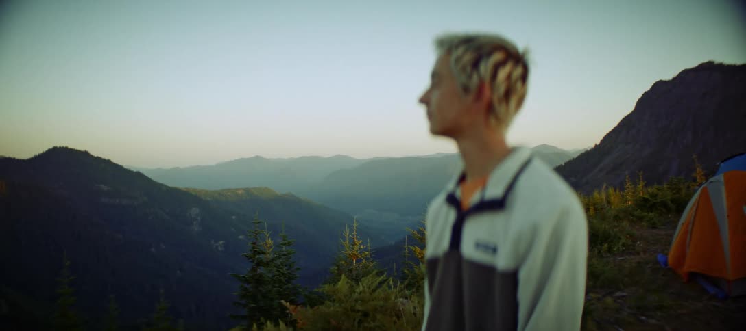 A man stands by a campsite overlooking mountains at dawn