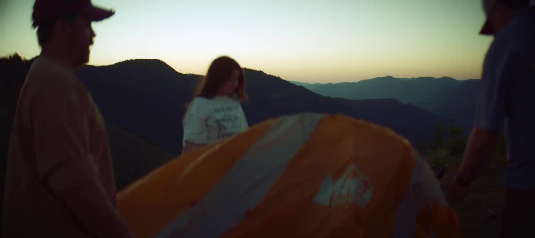 Friends setup a tent on a mountain overlooking a valley in a mountain range after dusk