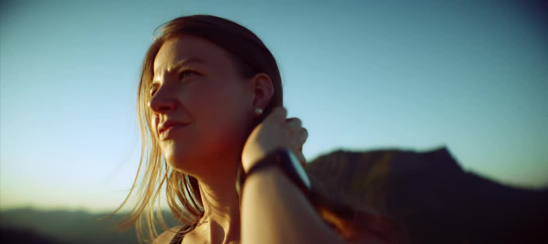 Woman standing outdoors with a mountain in the background on a windy day pushes her hair out of her face