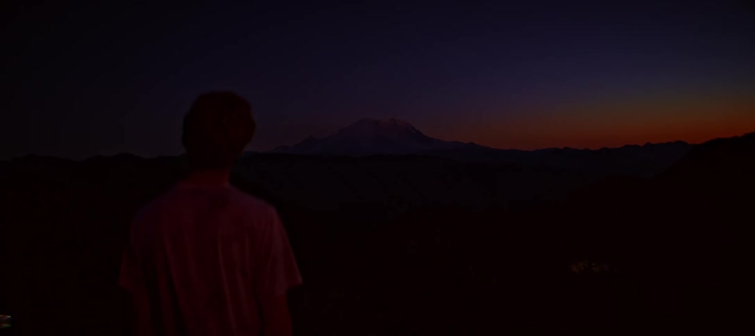 A person stands in silhouette gazing at a mountain at night