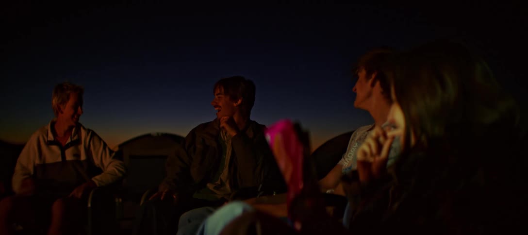 Group of friends sitting and talking at night with the silhouette of mountains on the horizon