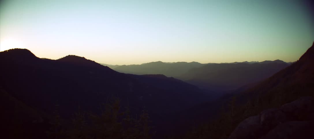 A landscape of mountains that are dark in the morning and the sky is getting light