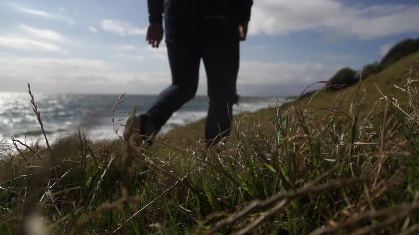 Person walking on a grassy hillside near the ocean