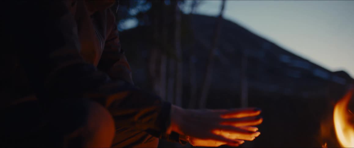 The woman warms her hands by the campfire