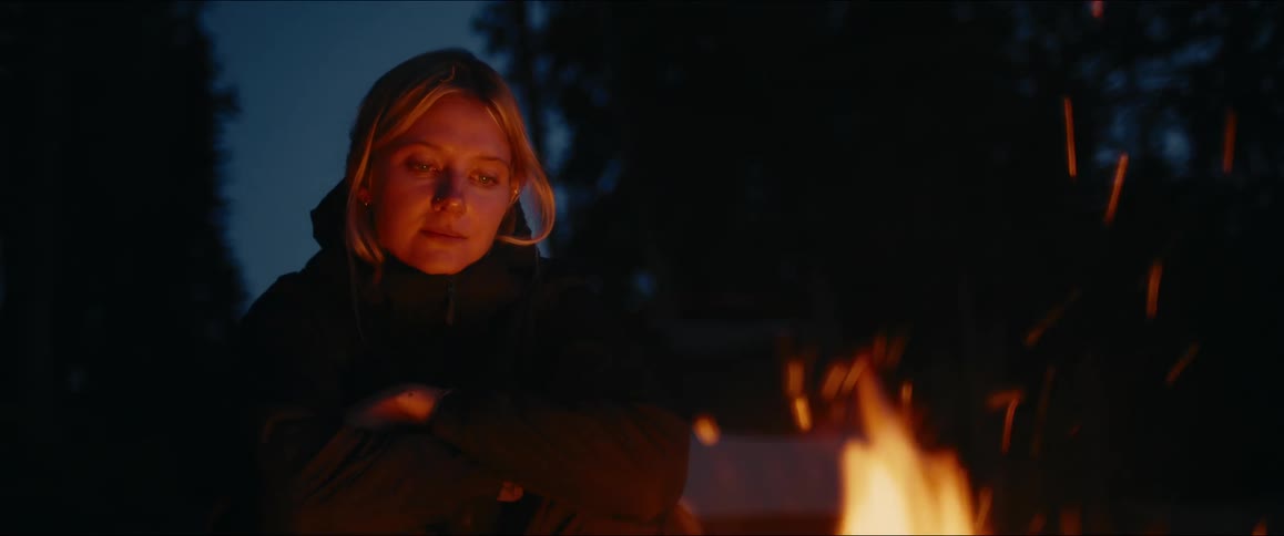 The woman is staring into the campfire