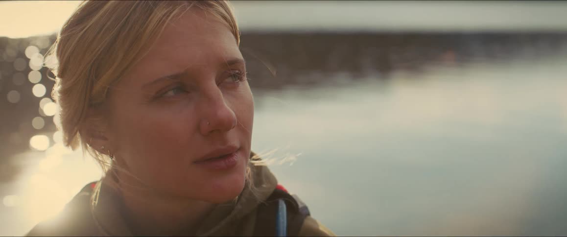 A closeup shot of a contemplative womans face outdoors in the cold as she looks thoughtfully into the distance while the sunlight flares and shifts