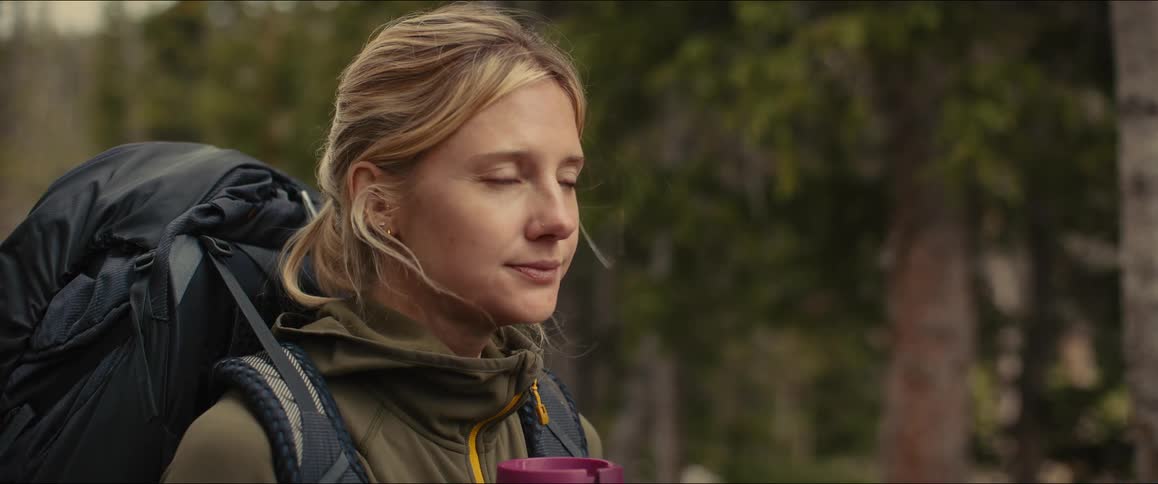 A woman drinks from a travel cup while hiking through a forest
