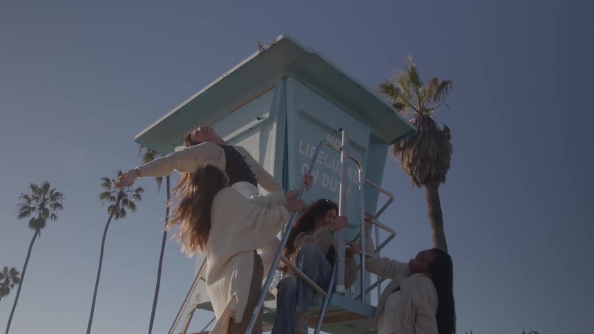 A group of friends playfully pose on a lifeguard tower at the beach
