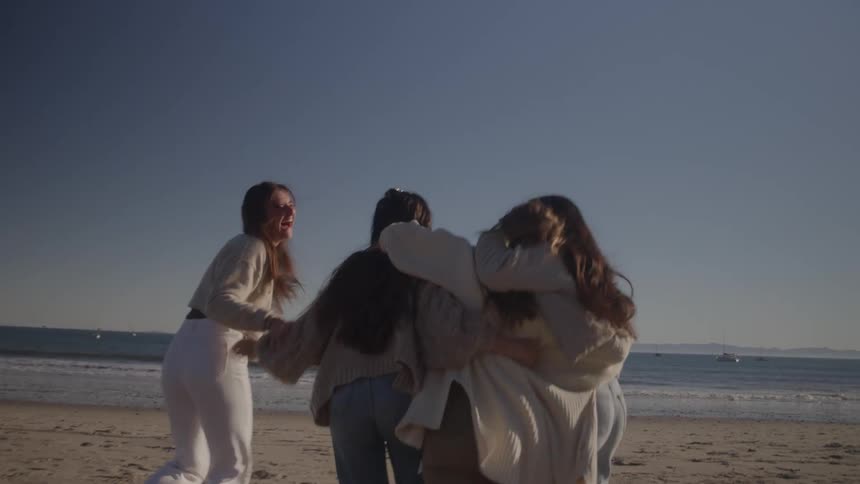Four female friends hugging each other excitedly while walking toward the beach at midday