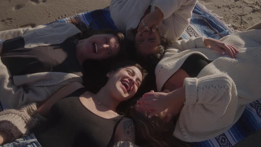 Four friends lying on a towel in the sand