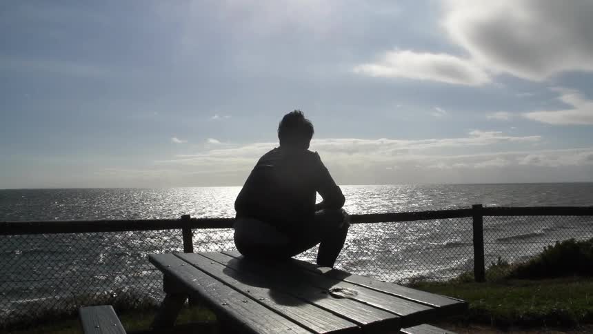 A man sits on a picnic table overlooking the ocean