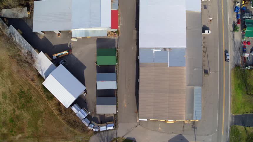 Industrial buildings and containers are next to a road with traffic surrounded by land