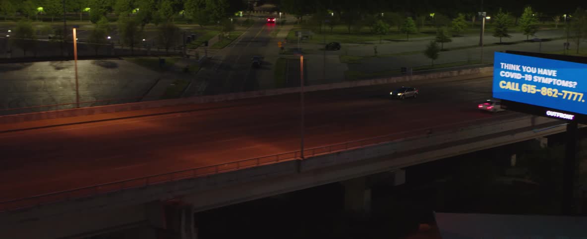 A lone car drives down an empty dimly lit road at night before encountering mild traffic
