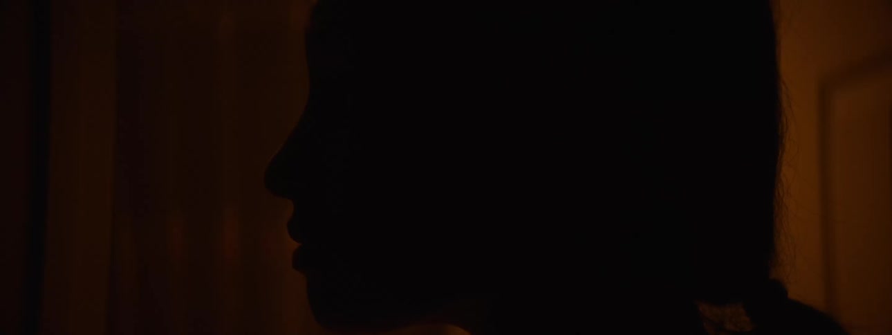 A close up shot of a womans head in an indoor setting with low light while she look to the side and the front