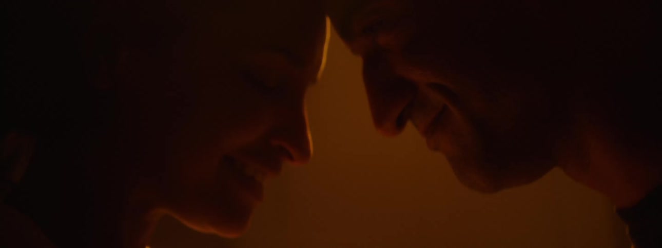 A man and woman smile while standing face to face and embracing
