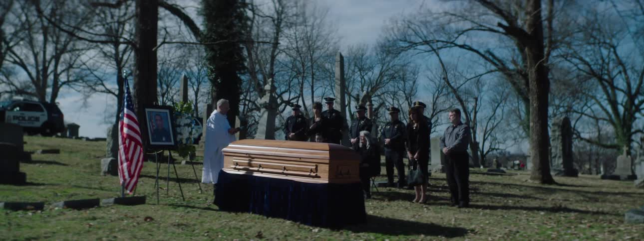 Mourners and uniformed officers gather solemnly around a casket during a cemetery funeral service