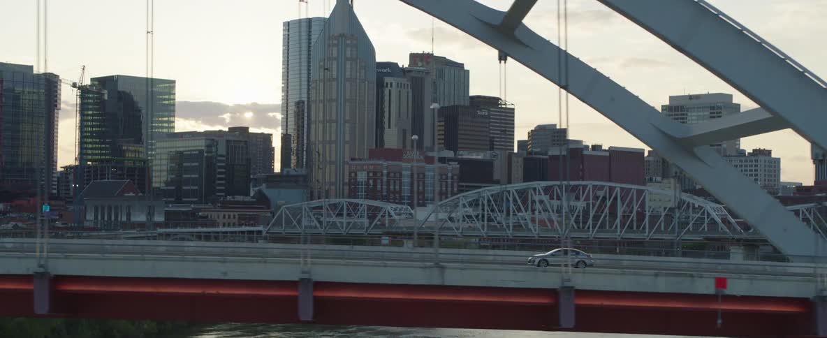 An aerial shot tracks cars on a city highway at dusk with the nashville skyline and bridges in the background