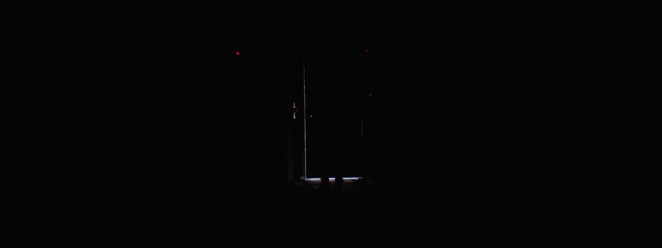 In the video a person walks down a long dark hallway with a bright light visible at the end the persons silhouette is cast in the doorway as they stop seemingly to push on the door