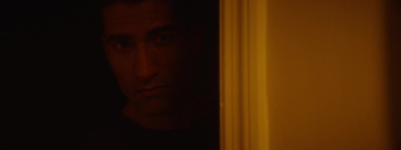 A video game scene of a man with a serious expression peering cautiously through a doorway lit by warm golden light