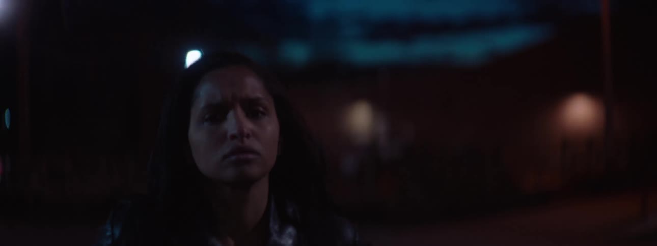 A woman is walking at night on a street then comes next to a car