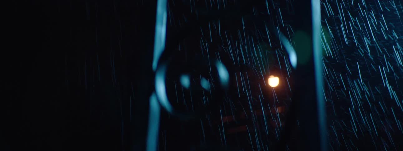 View through a metal gate of a light in the background on a rainy day at night